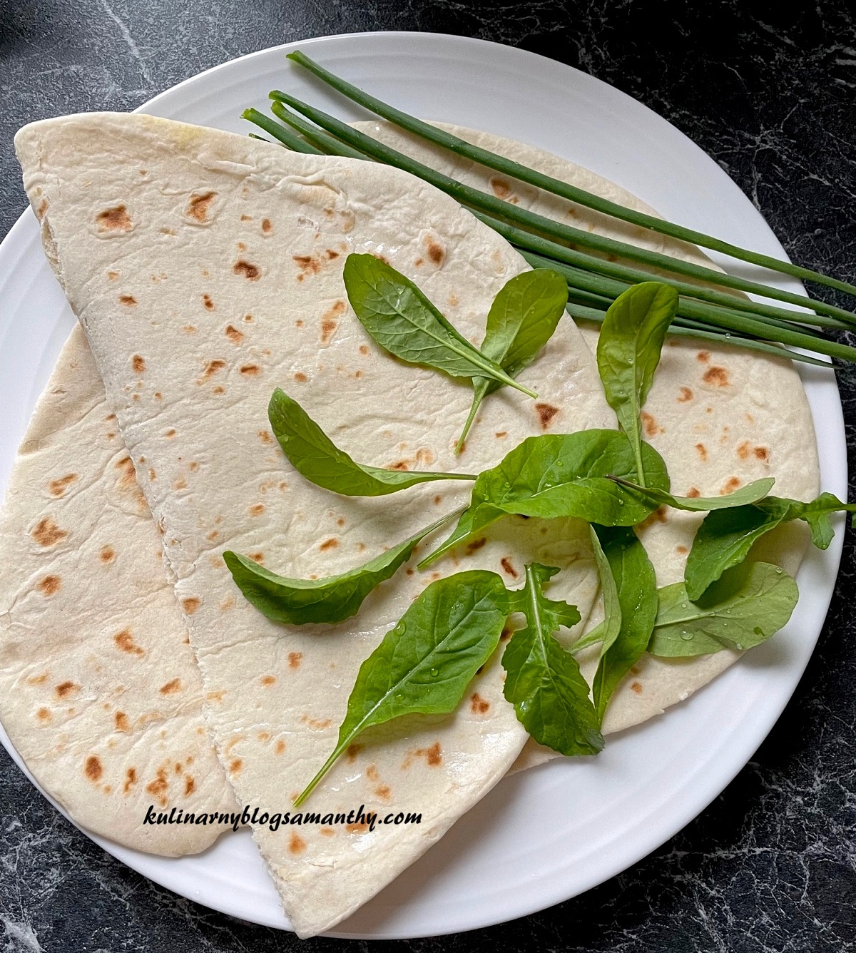 Dormowa tortilla z rukolą i szczypiorkiem na białym talerzu